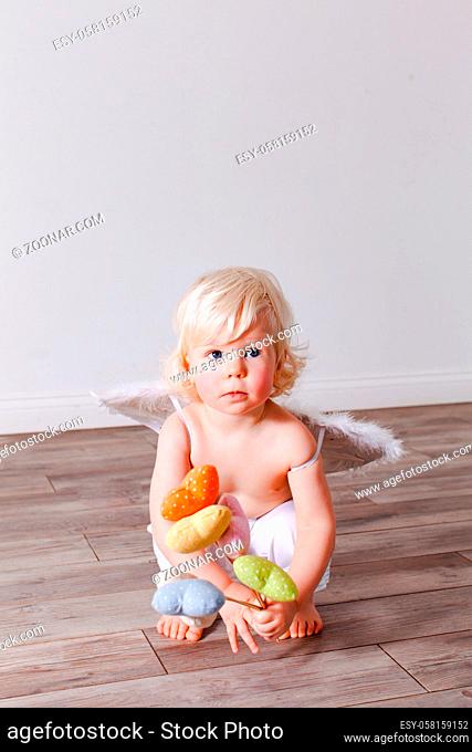 Adorable baby with angel wings holds textile handmade hearts on the sticks