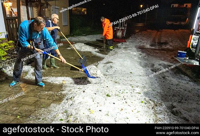 09 September 2022, Mecklenburg-Western Pomerania, Stralsund: Men shovel hailstones from the sidewalk with snow pushers. Cellars and apartments were flooded by...