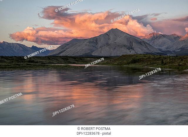 The midnight sun shines on the mountains and clouds lining the Wind River in the Peel watershed; Yukon, Canada