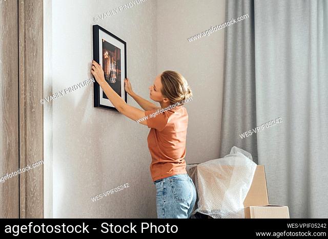Young woman putting picture frame on wall at new home