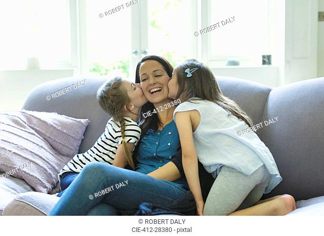 Daughters kissing mother’s cheeks on living room sofa