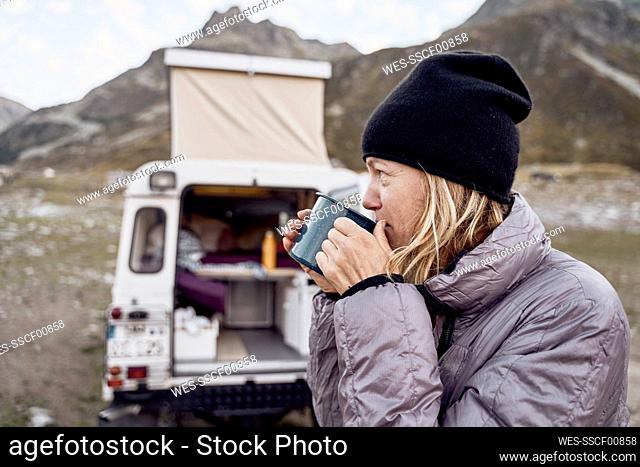 Thoughtful tourist having tea by motor home, Splugen Pass, Sondrio, Italy