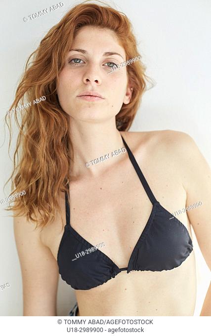 Half length portrait of young redhead woman wearing a black bikini, looking at camera