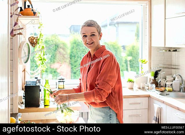 Smiling woman holding herbs in kitchen at home
