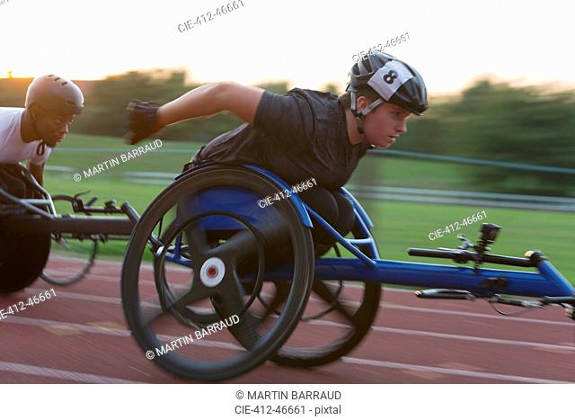 Determined young female paraplegic athlete speeding along sports track in wheelchair race