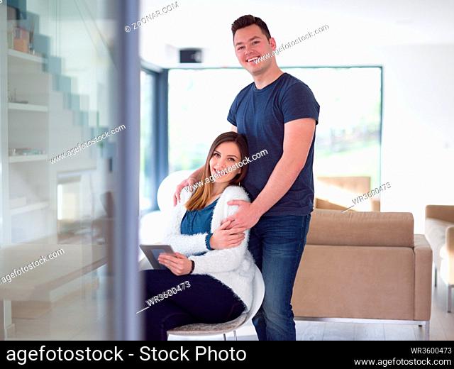 Young couple using tablet computer at luxury home together, looking at screen, smiling