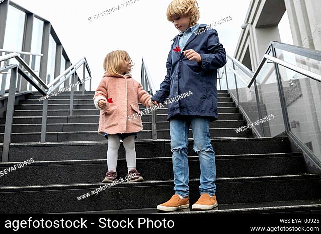 Brother and sister with lollipops standing on stairs on a rainy day