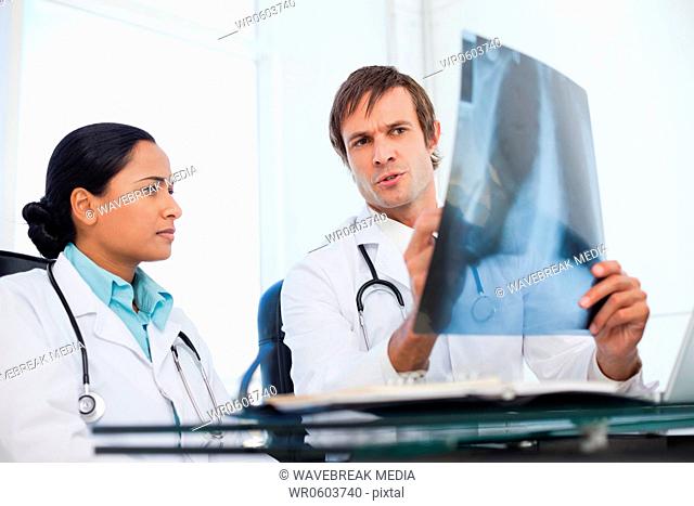 Serious doctors sitting at a desk side by side while looking at an x-ray