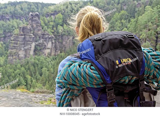 Woman with backpack and climbing rope looking at rocks, Elbsandsteingebirge Elbe Sandstone Mountains, Saxony, Germany, Europe