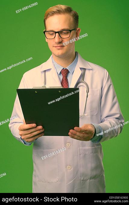Studio shot of young handsome man doctor with blond hair against green background