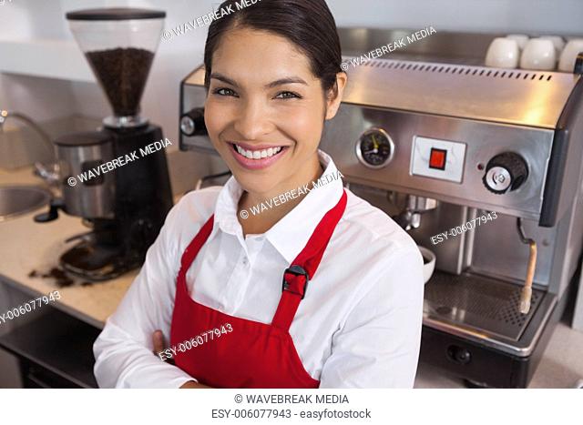 Happy young barista leaning against counter smiling at camera
