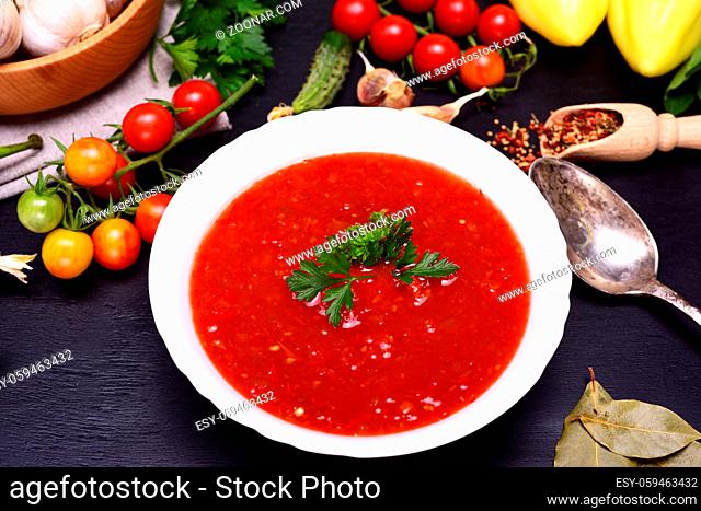 Gazpacho Spanish cold soup in a white round ceramic plate in the midst of fresh vegetables ingredients, top view