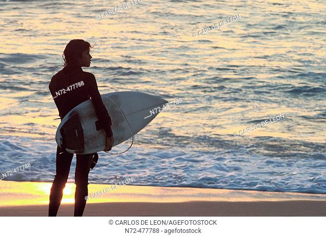 After a long day surfing a young surfer is watching the sunset over  the Pacific Ocean, Baja California, Mexico