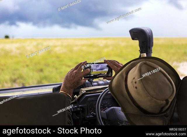 A safari guide taking smart phone picture of approaching storm clouds