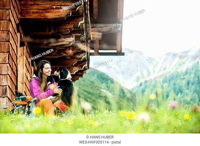 Austria, Altenmarkt-Zauchensee, young woman and dog in front of an Alpin cabin