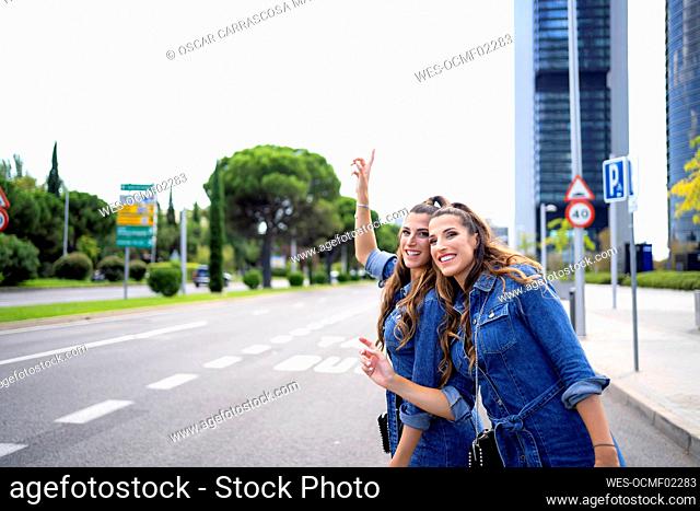 Smiling twin sisters standing on road in city