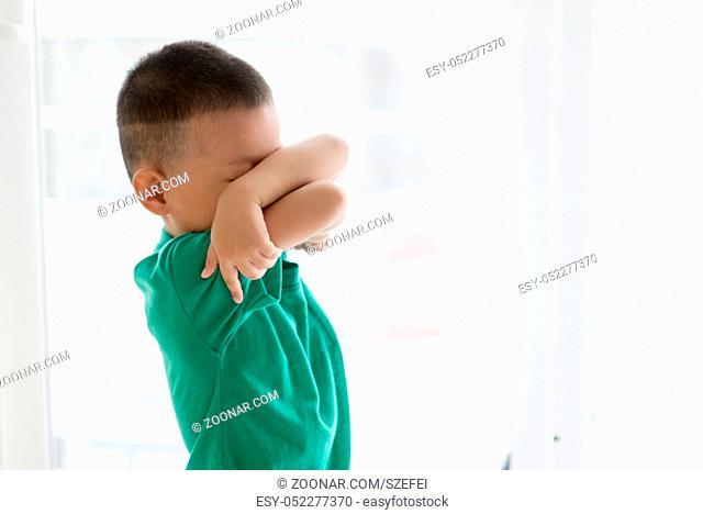 Young child at home. Playful Asian boy covering his face