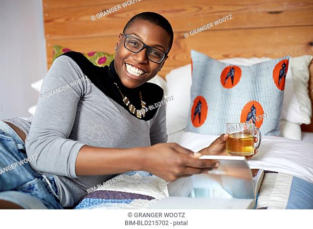 Mixed race woman drinking tea and reading on bed