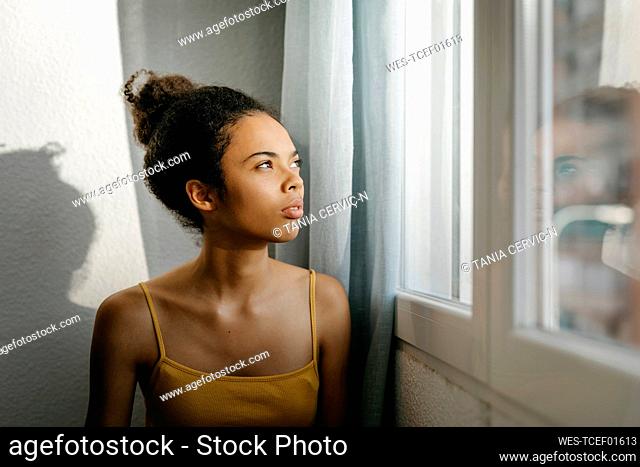 Thoughtful young woman looking through window at home