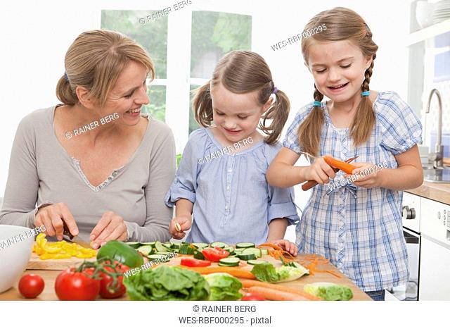 Germany, Munich, Mother and daughters (4-7) chopping vegetables