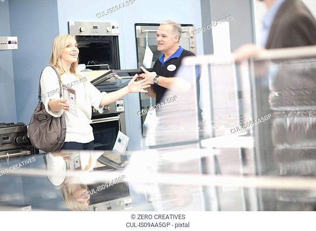 Young woman and salesman looking at ovens in showroom