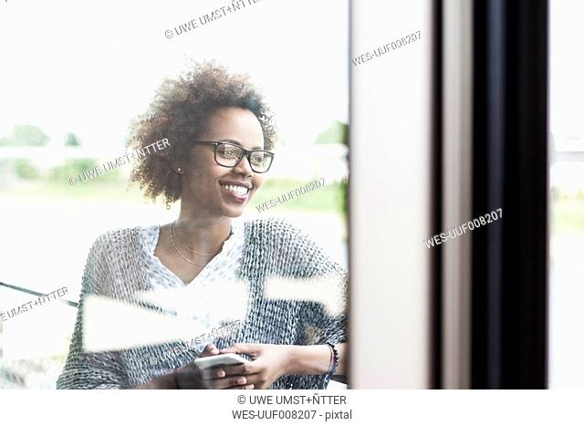 Smiling woman with smartphone standing on balcony looking at distance