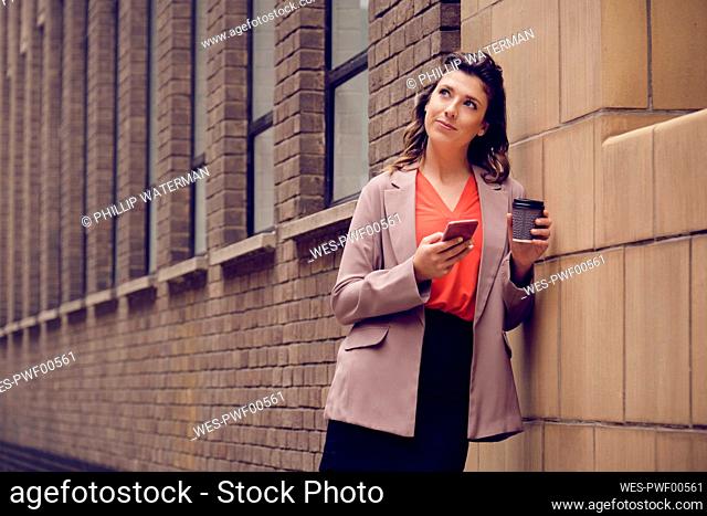 Thoughtful businesswoman with smart phone and coffee cup