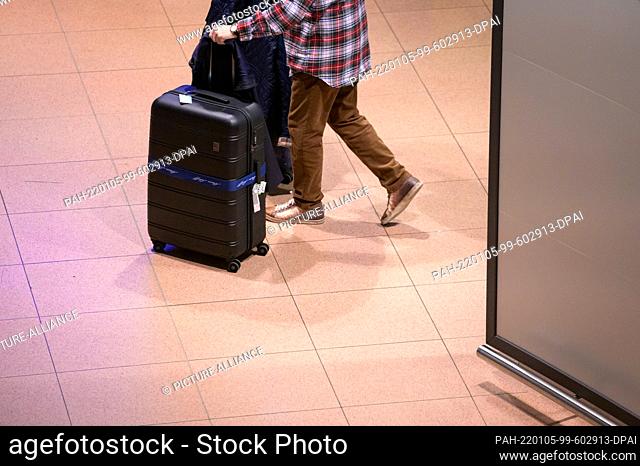 04 January 2022, Hamburg: Returning passenger of the cruise ship ""Aidanova"" walks through the arrivals area of Hamburg airport with his suitcases during the...