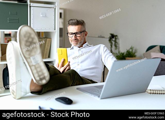 Businessman with feet up using mobile phone at desk
