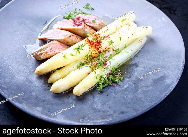 Fried Iberian pork fillet sliced with blanched white asparagus and herbs with spice as closeup on a modern design plate