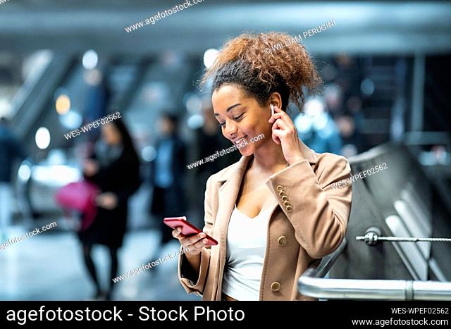 Smiling young woman with cell phone and earbuds at subway station