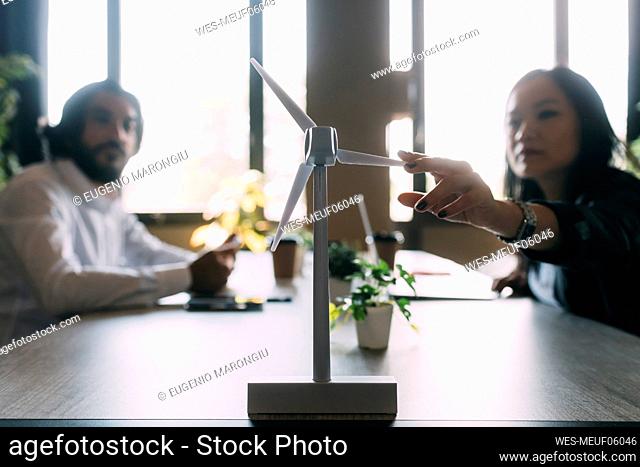 Businesswoman discussing over wind turbine model with colleague at work place