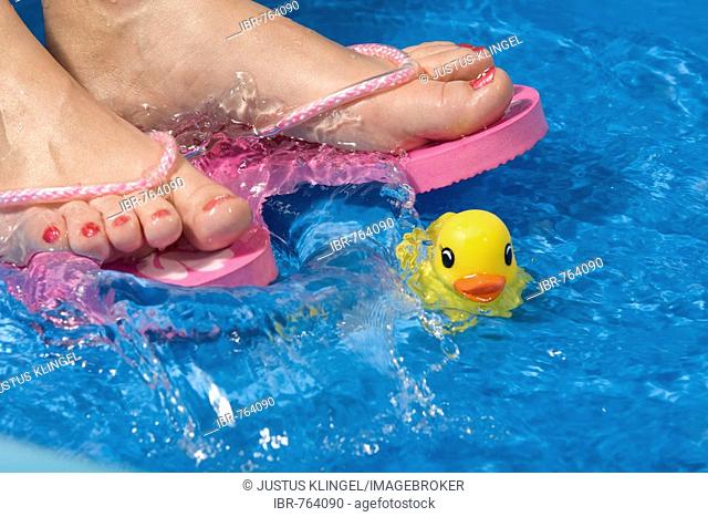 Feet wearing flip-flops in a paddling pool with a rubber duck