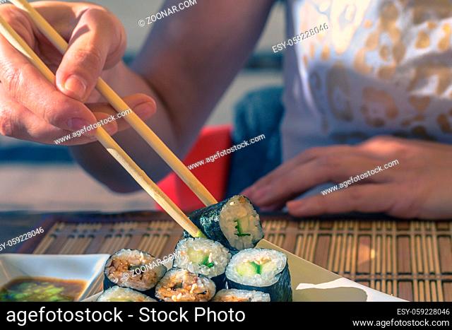 Woman with japan sticks eats sushi in street cafe