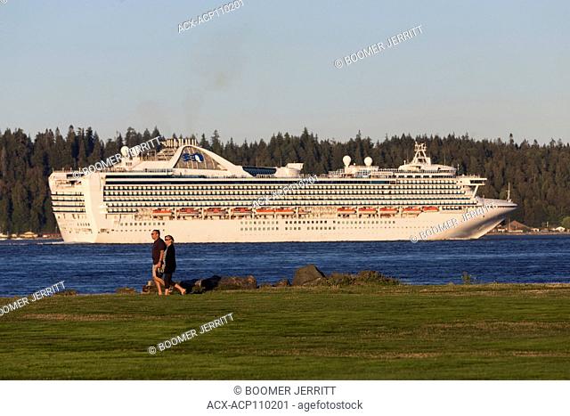 A couple strolls along a walkway on Tyee Spit while a princess cruiseline ship passes through Discovery Passage, Campbell River, Vancouver Island