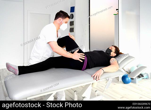 Woman lying on massage table while his physical therapist doing special exercises for physical therapy for sciatica and pinched nerve problems