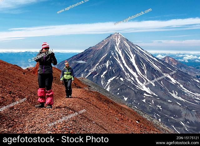 AVACHA VOLCANO, KAMCHATKA PENINSULA, RUSSIA - AUG 7, 2014: Two young women tourists are walking along a mountain hiking trail on edge of crater of active...