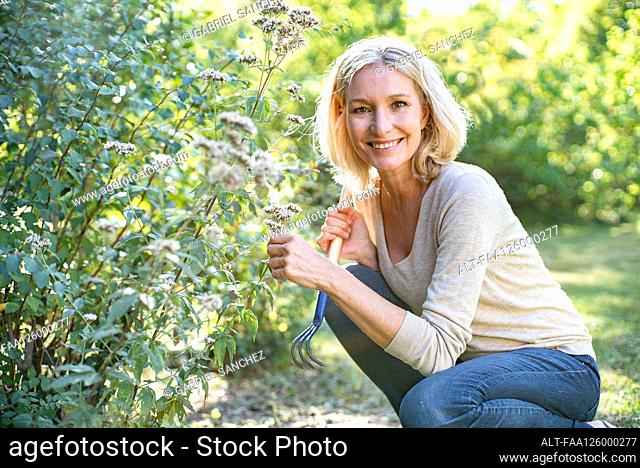 Portrait of smiling mature woman holding flowers in backyard