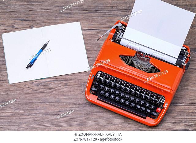 Das Foto zeigt eine Schreibmschine und ein Notizbuch auf einem Holztisch