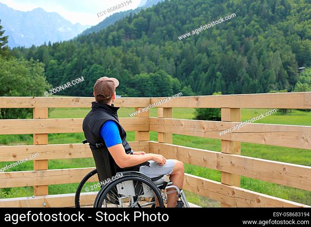 Disabled young man on a wheelchair on a wooden bridge path enjoying in nature looking at beautiful view