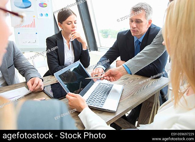 Team of business people at meeting in office discuss financial data using laptop