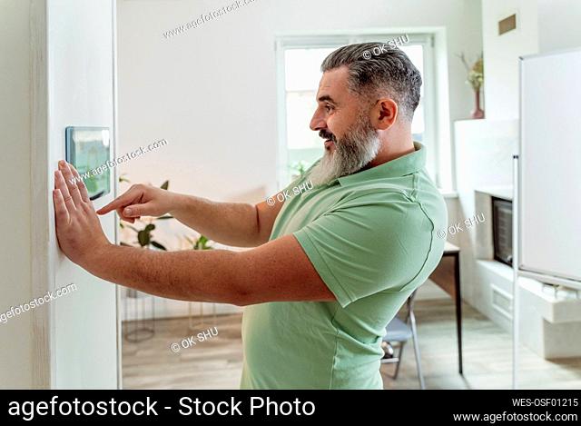 Smiling man using smart home application through tablet PC mounted on wall