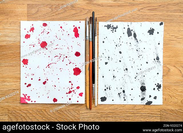 Two piece of papers spotted with ink and brushes in a wooden background