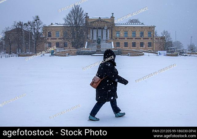 05 December 2023, Mecklenburg-Western Pomerania, Schwerin: A woman walks across the Old Garden in front of the State Museum in snowfall