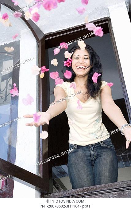 Young woman throwing flowers in air through a window