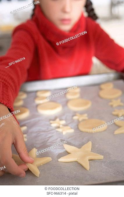 Girl placing cut-out biscuits on baking parchment