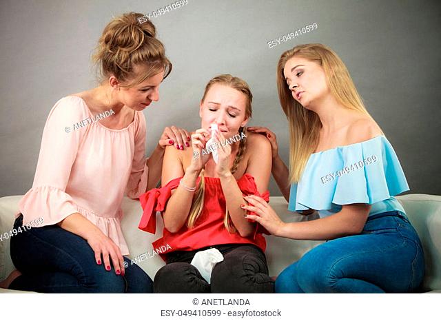 Female women comforting her woman friend while she is having cold flue blowing runny nose into paper tissue
