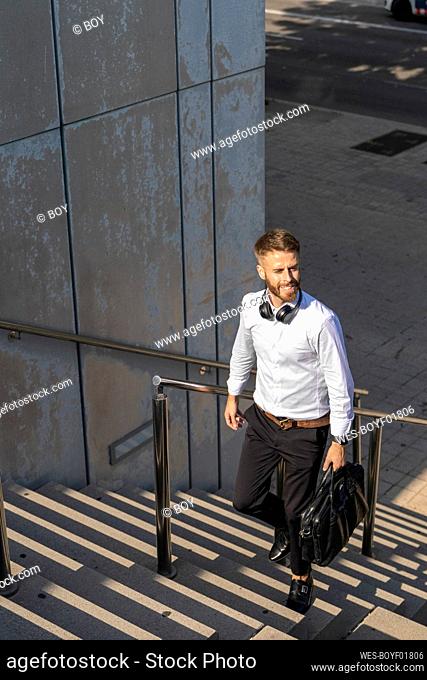 Smiling businessman looking away while walking with briefcase on steps