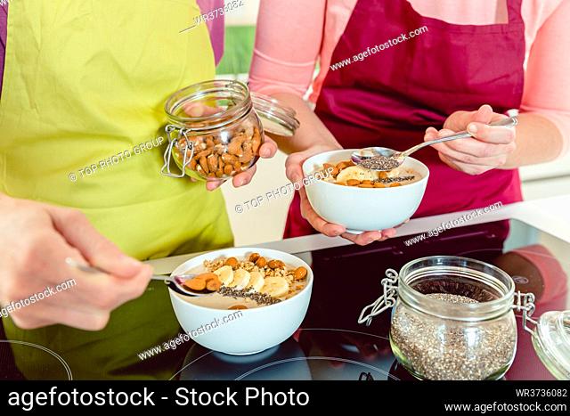 Two woman adding almonds and chia seeds to healthy oatmeal breakfast in the bowl