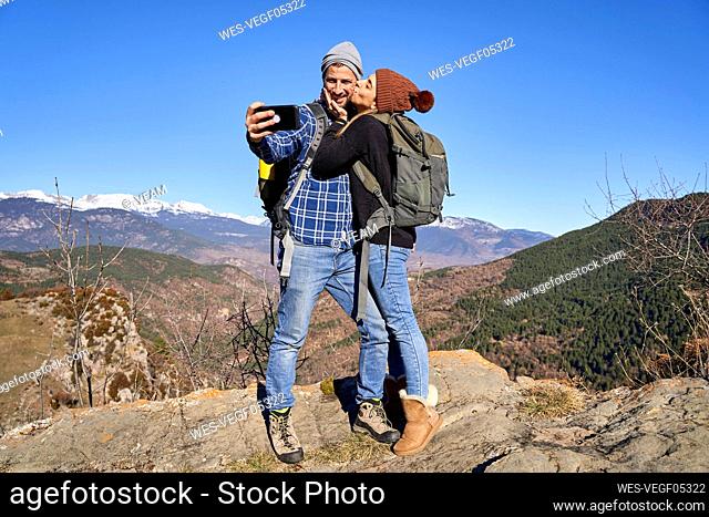 Woman kissing boyfriend taking selfie through smart phone on sunny day